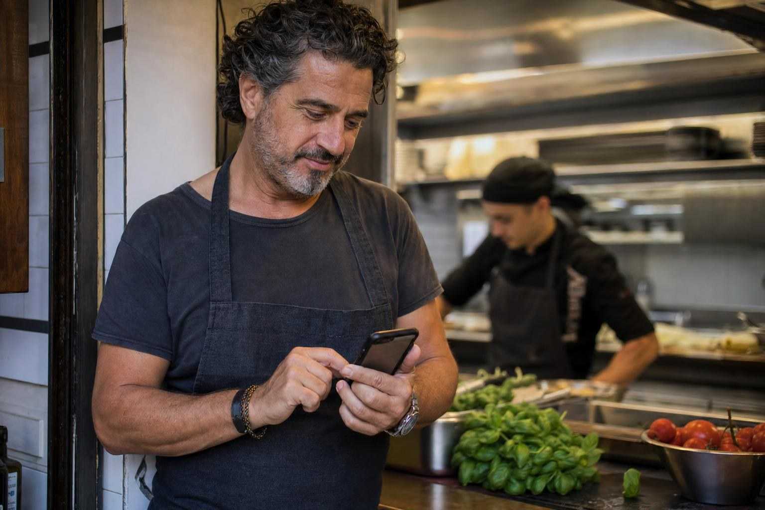 A restaurant owner updating his menu from a phone at the kitchen pass